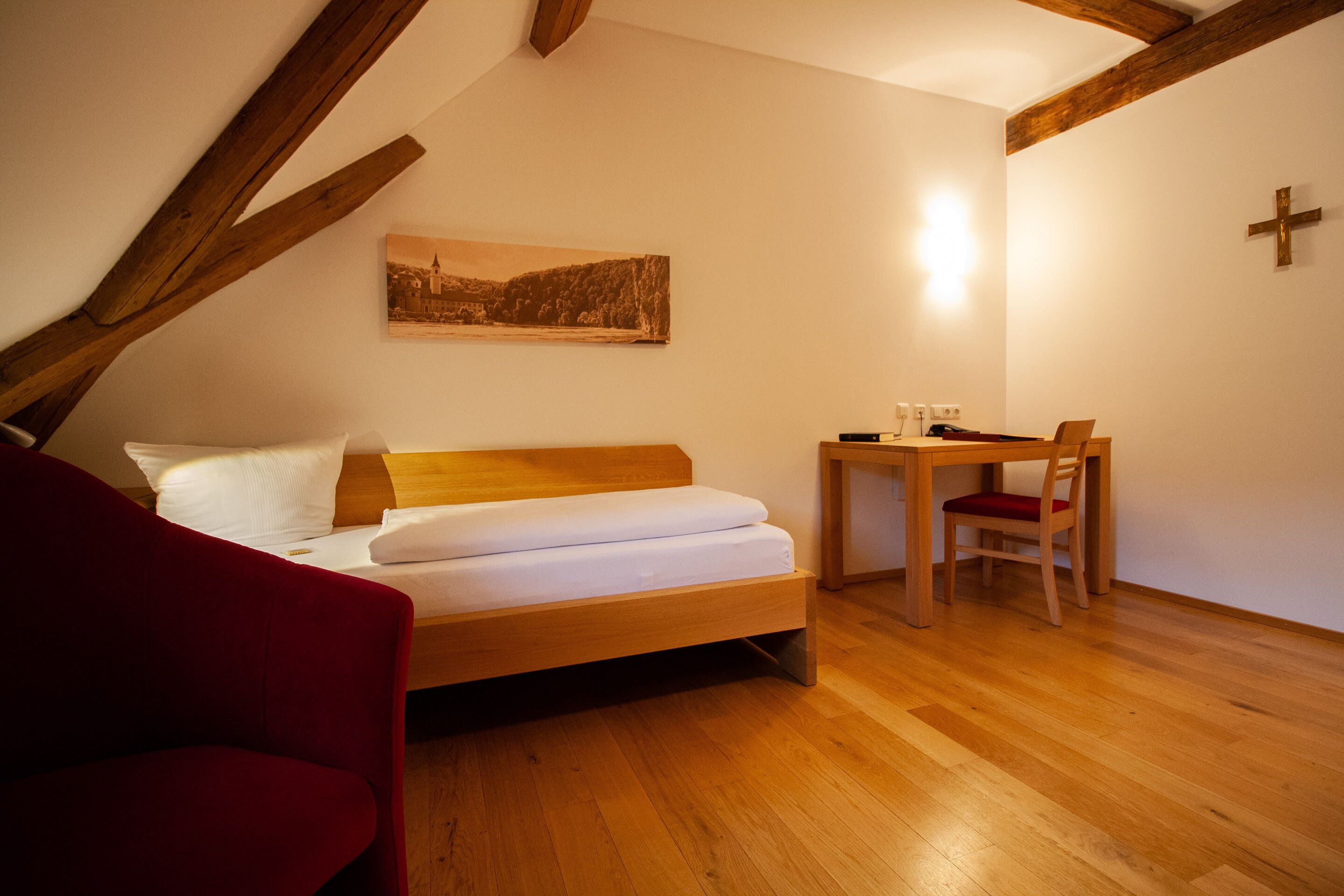 Un dormitorio con una cama de madera, un escritorio con una silla y una cruz en la pared.
