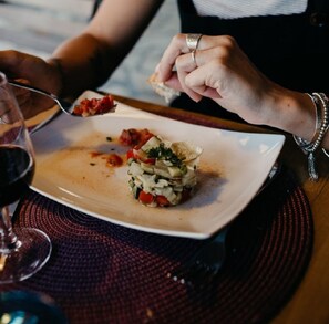 Iemand eet een gerecht met een vork, een glas rode wijn en een geweven placemat op een tafel.
