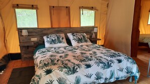 Een tentruimte met een bed, houten hoofdeinde en twee ramen.