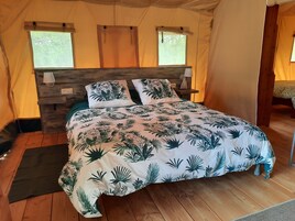 Una habitación con carpa, una cama, cabecera de madera y dos ventanas.