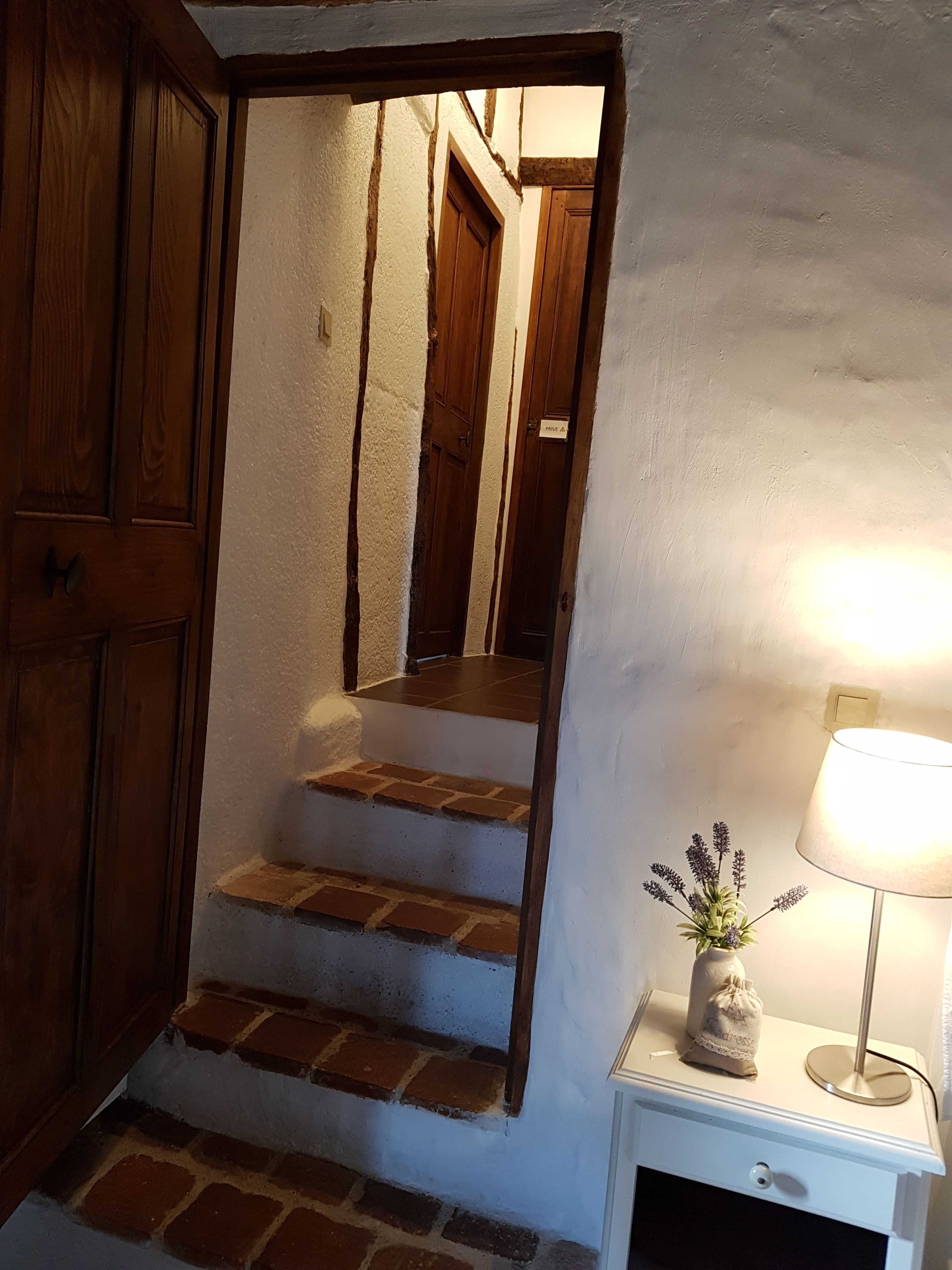 A staircase with wooden steps and a white wall. There is a nightstand with a lamp and a small plant.