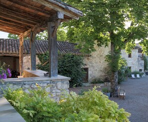 Experience the tranquil ambiance of this historic residence, featuring a shaded seating area beneath a traditional roof and surrounded by lush greenery.