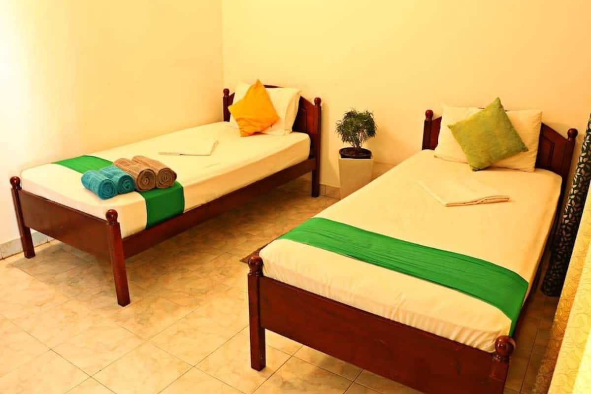 Dos camas individuales con estructura de madera, cada una con cubrecama verde y blanco, almohadas y toallas enrolladas.