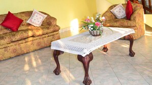 Una sala de estar con una escalera, una araña, un conjunto de sofás y una mesa con flores.