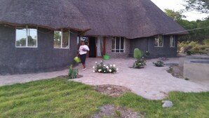 A thatched-roof house with a paved entrance, a small garden with white flowers, and a cactus plant. - Beatrice Lodges and Conference Centre (Beatrice)