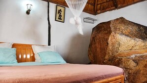 A bedroom with a wooden bed, a large stone wall, and a mosquito net above the bed. - Beatrice Lodges and Conference Centre (Beatrice)