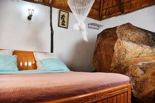Un dormitorio con una cama de madera, una pared de piedra grande y un mosquitero sobre la cama.