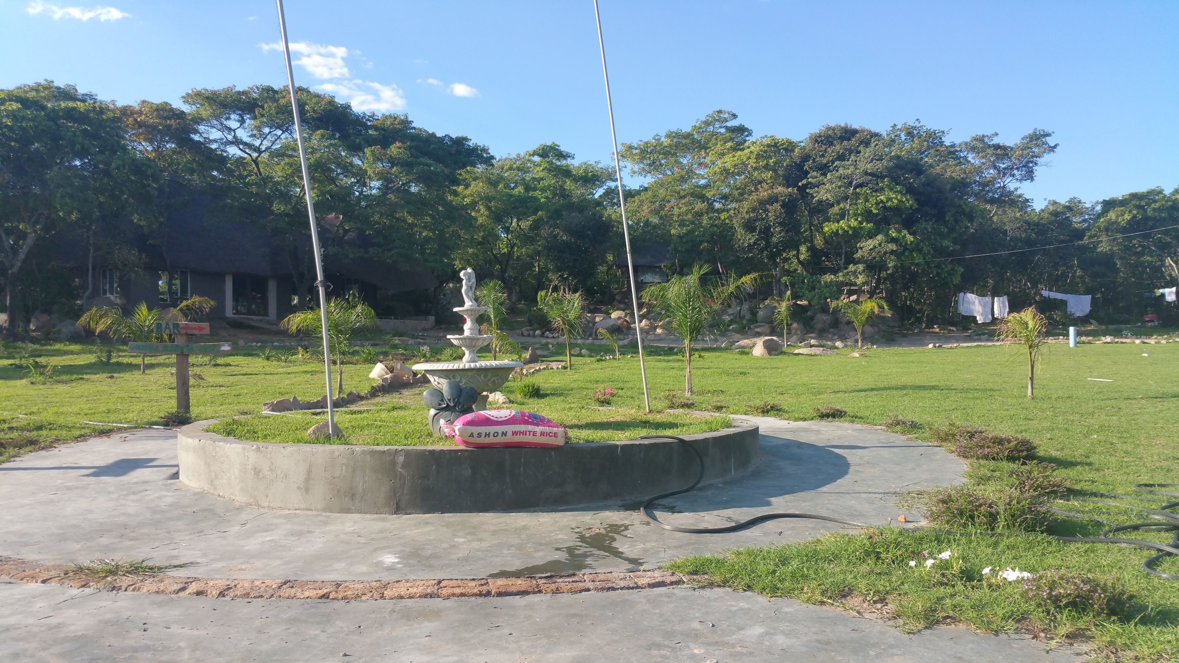 Egy park, amelyben van egy szökőkút, egy „BARG” feliratú tábla és egy betonsáv.