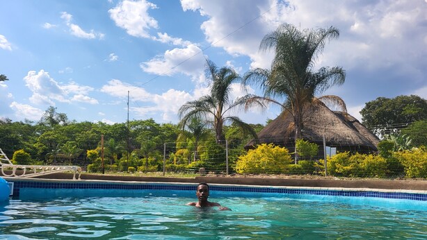 A swimming pool with clear water, surrounded by lush greenery and a thatched-roof structure. - Beatrice Lodges and Conference Centre (Beatrice)