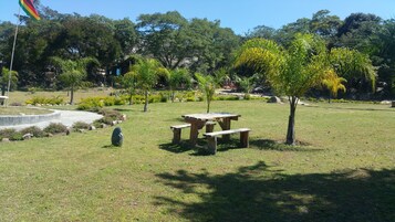 Un área de picnic con una mesa y bancos, rodeada de césped y árboles.