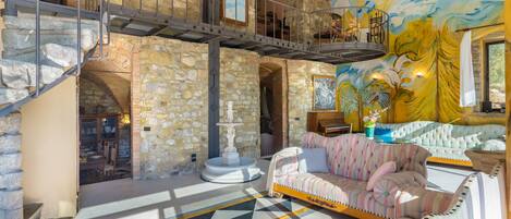 A spacious living area with a stone wall, a piano, a sofa, and a staircase.