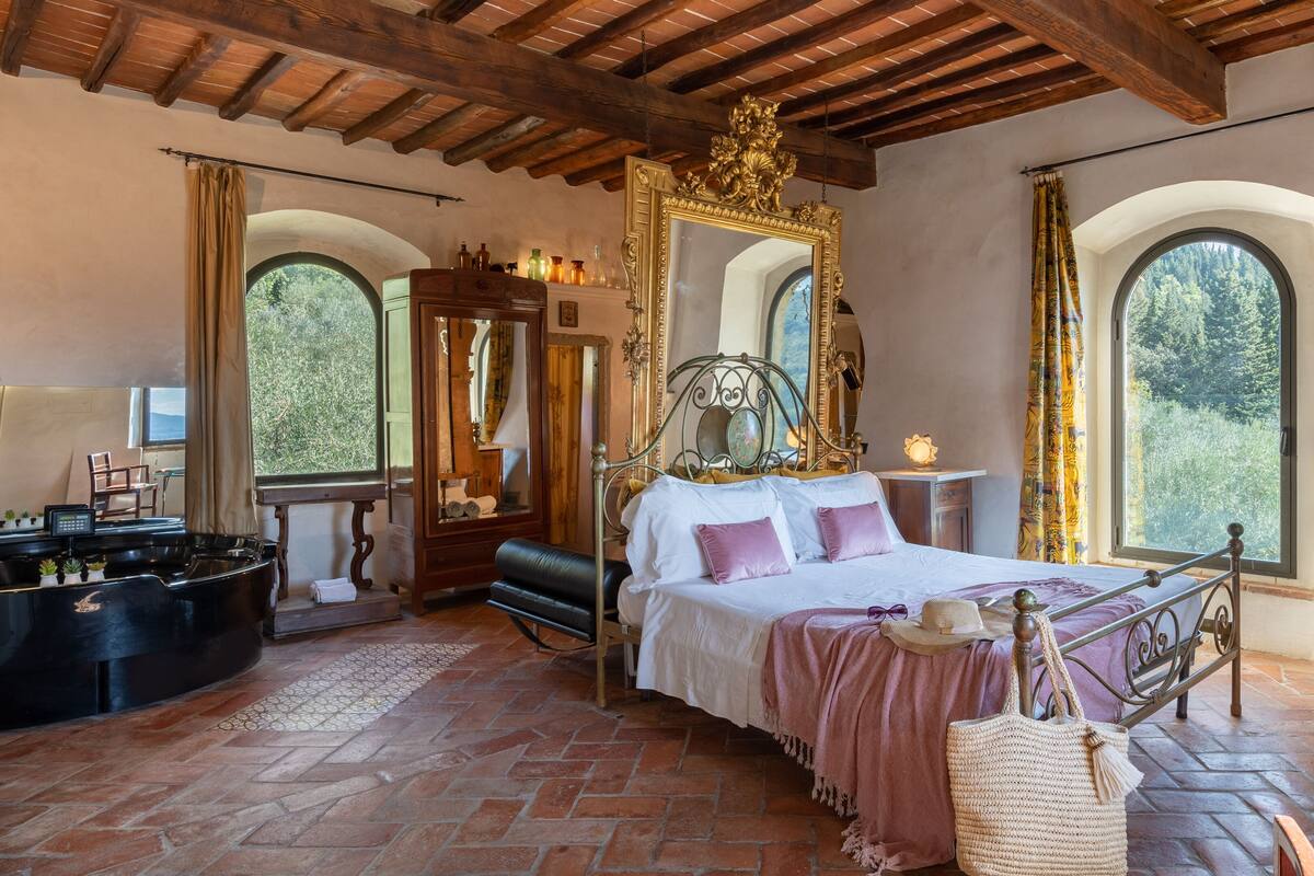 A bedroom with a bed, a piano, a mirror, and a fireplace.