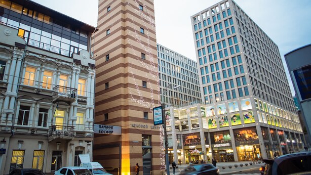 Un edificio de varios pisos con una torre de reloj, ventanas amplias y un cartel que indica un establecimiento comercial.