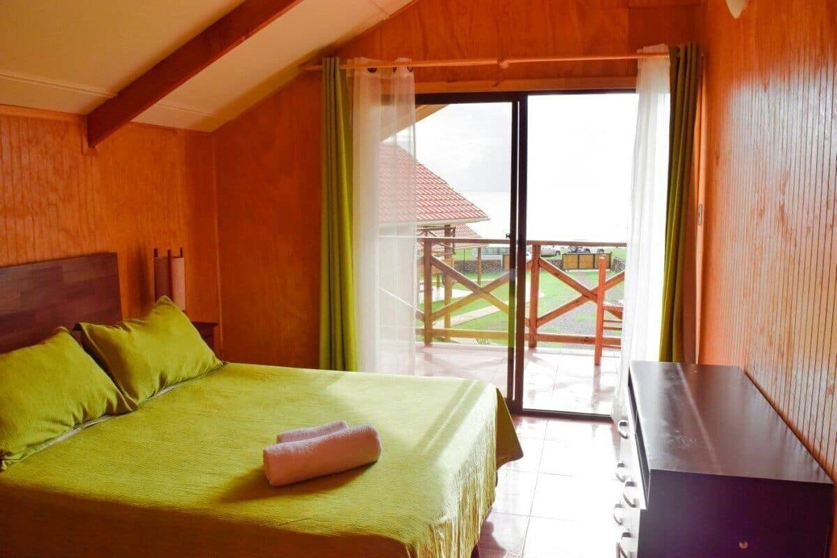 A room with a bed, a desk, and a view of a wooden deck and building.