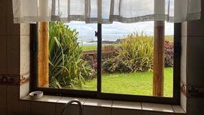 Une fenêtre de cuisine donnant sur un jardin et l’océan.