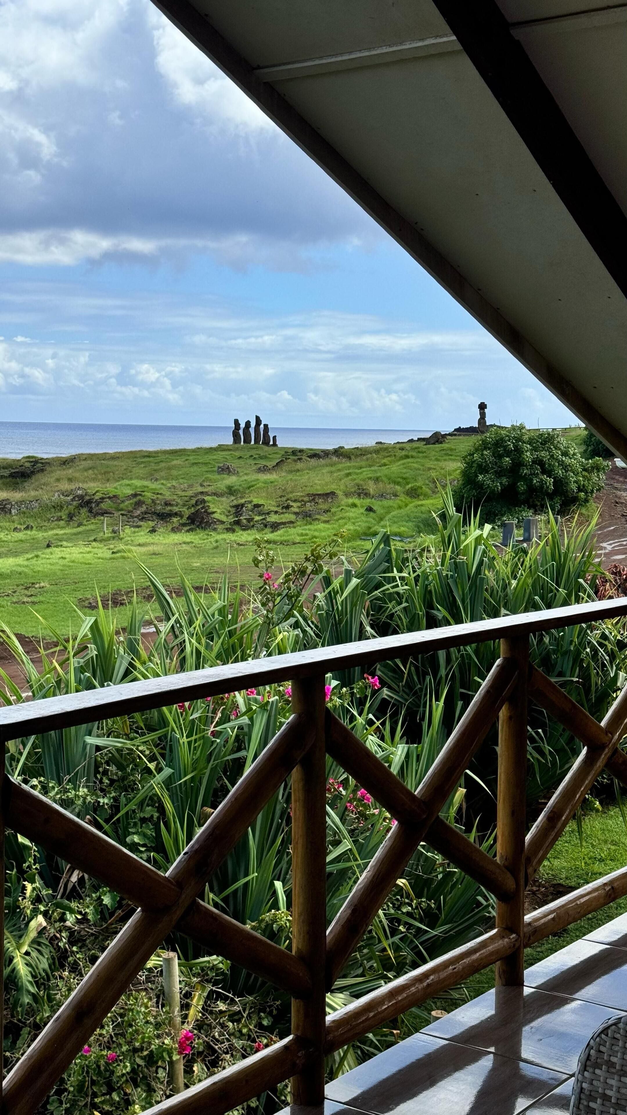 Vista desde un espacio cubierto sobre un paisaje con césped, un monumento de piedra y una estructura alta en la distancia.