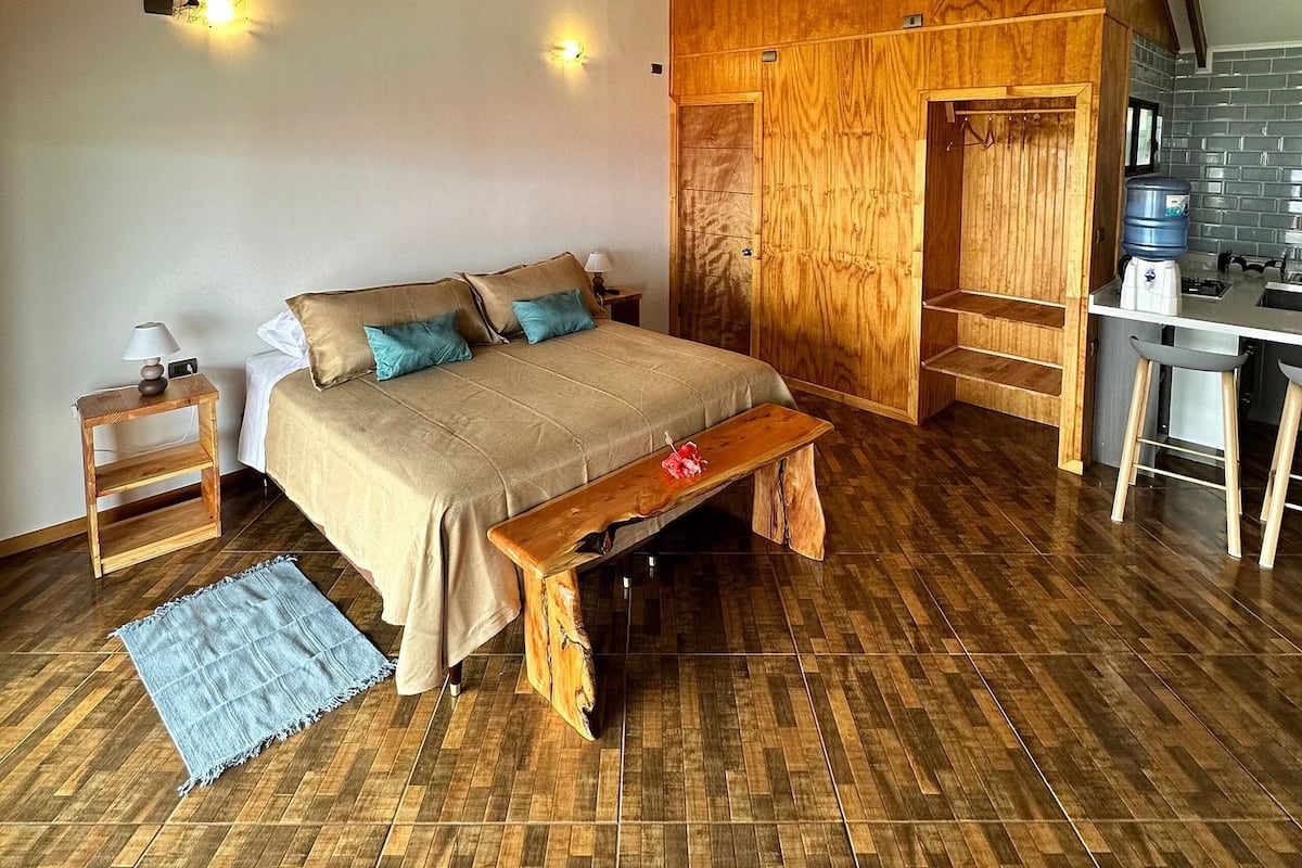 A bedroom with a wooden bed, a nightstand, a bench, and a small table with a lamp.