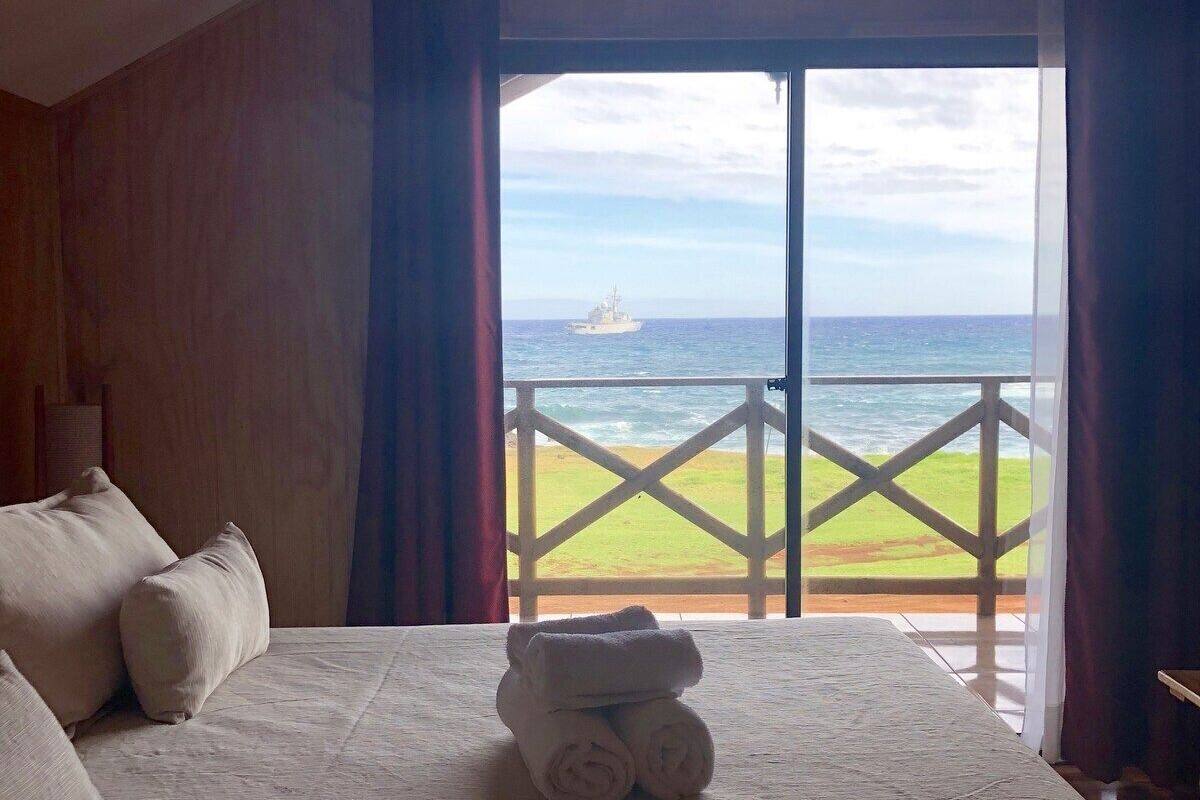 A bedroom with a bed, pillows, and a view of the ocean through a balcony.