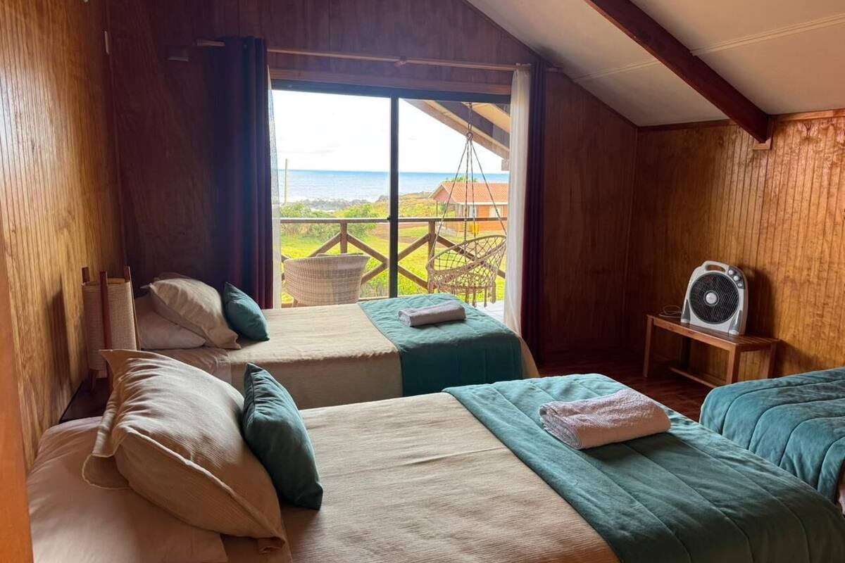 A room with two beds, a fan, and a view of the ocean.