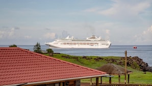 Une maison avec un toit rouge, une véranda et une vue sur un navire de croisière au loin.
