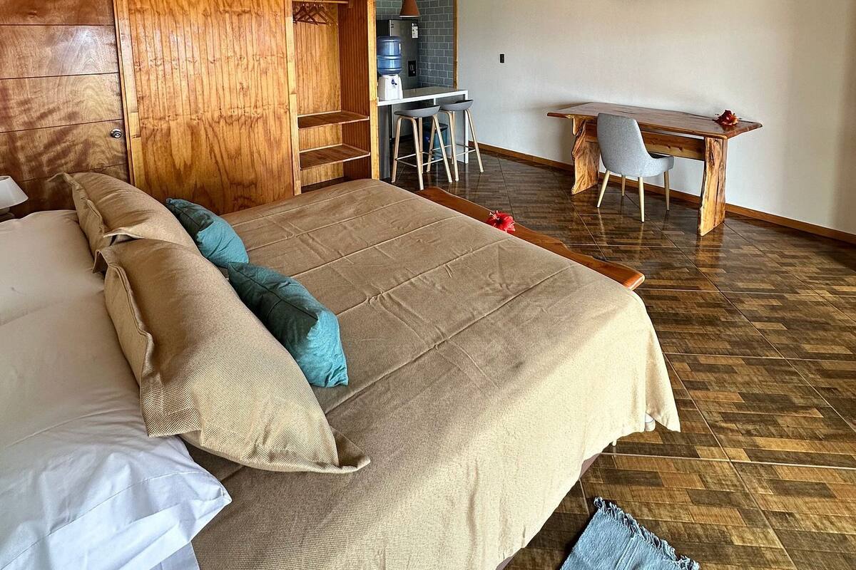 A bedroom with a large bed, wooden headboard, a desk, and a TV mounted on the wall.