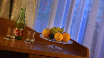 Una mesa de madera con una botella de agua, dos copas para shots y un plato de frutas con naranjas, uvas y una ciruela.