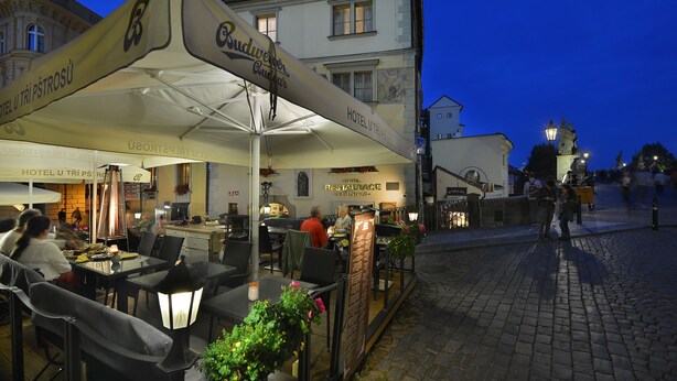 An outdoor café with tables and chairs, a large umbrella, and a sign for "Budweiser." - Hotel U Tri Pstrosu (Prague)