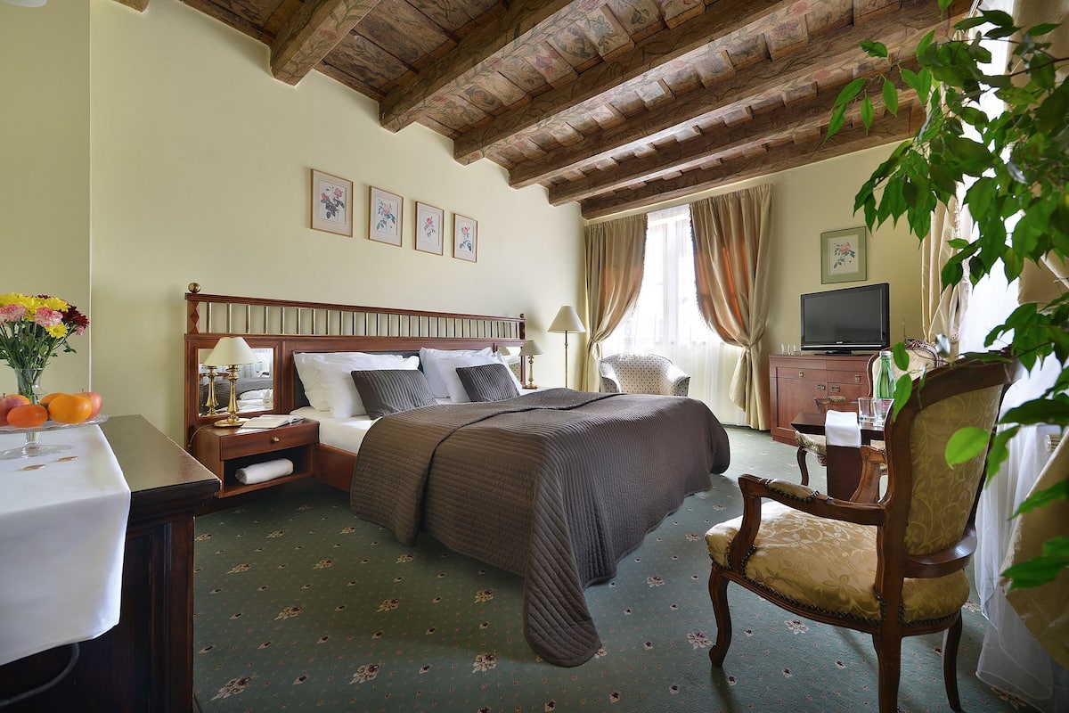 Una habitación de hotel con una cama, una silla de madera, un escritorio con una lámpara y un televisor.