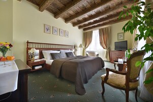 Quarto de hotel com cama, uma cadeira de madeira, escrivaninha com luminária e televisão.