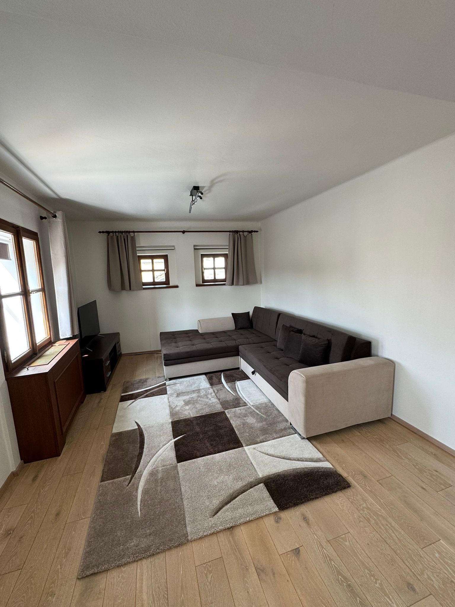 Een moderne woonkamer met een hoekbank, een flatscreen televisie en een houten vloer.