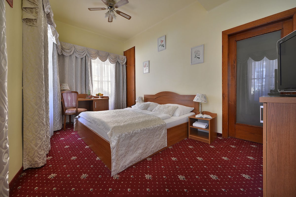 Una habitación de hotel con cama, escritorio, silla, mesita de noche y televisor.