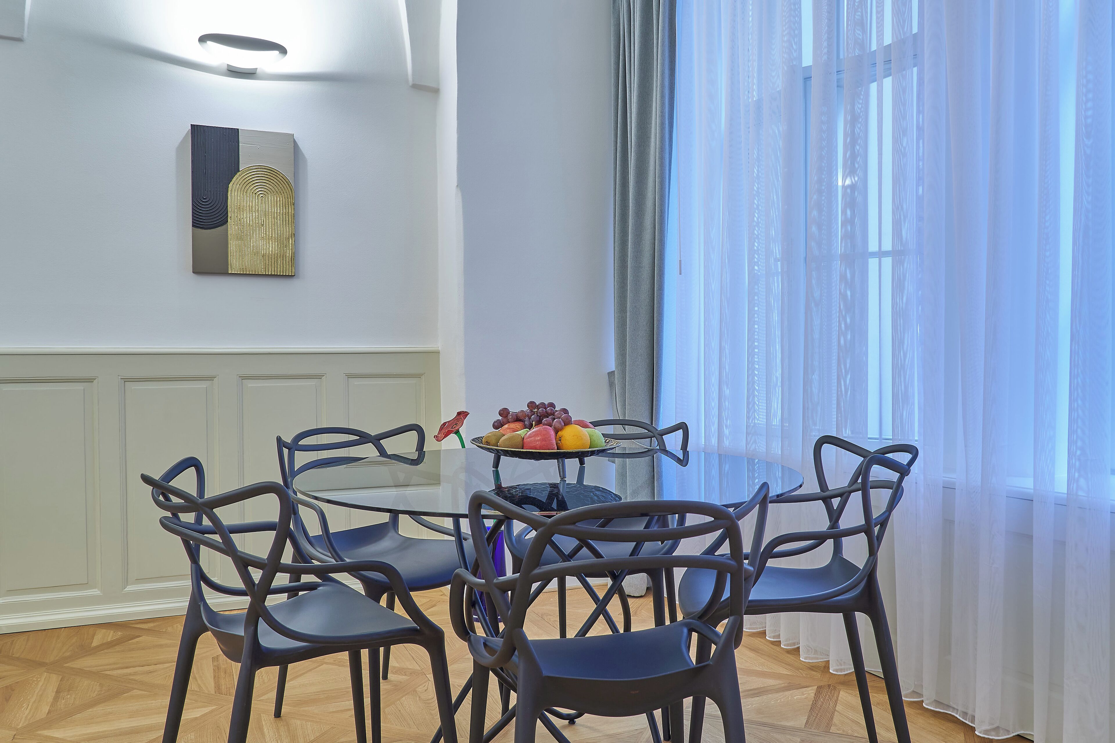A dining area with a round table, four chairs, and a fruit bowl.