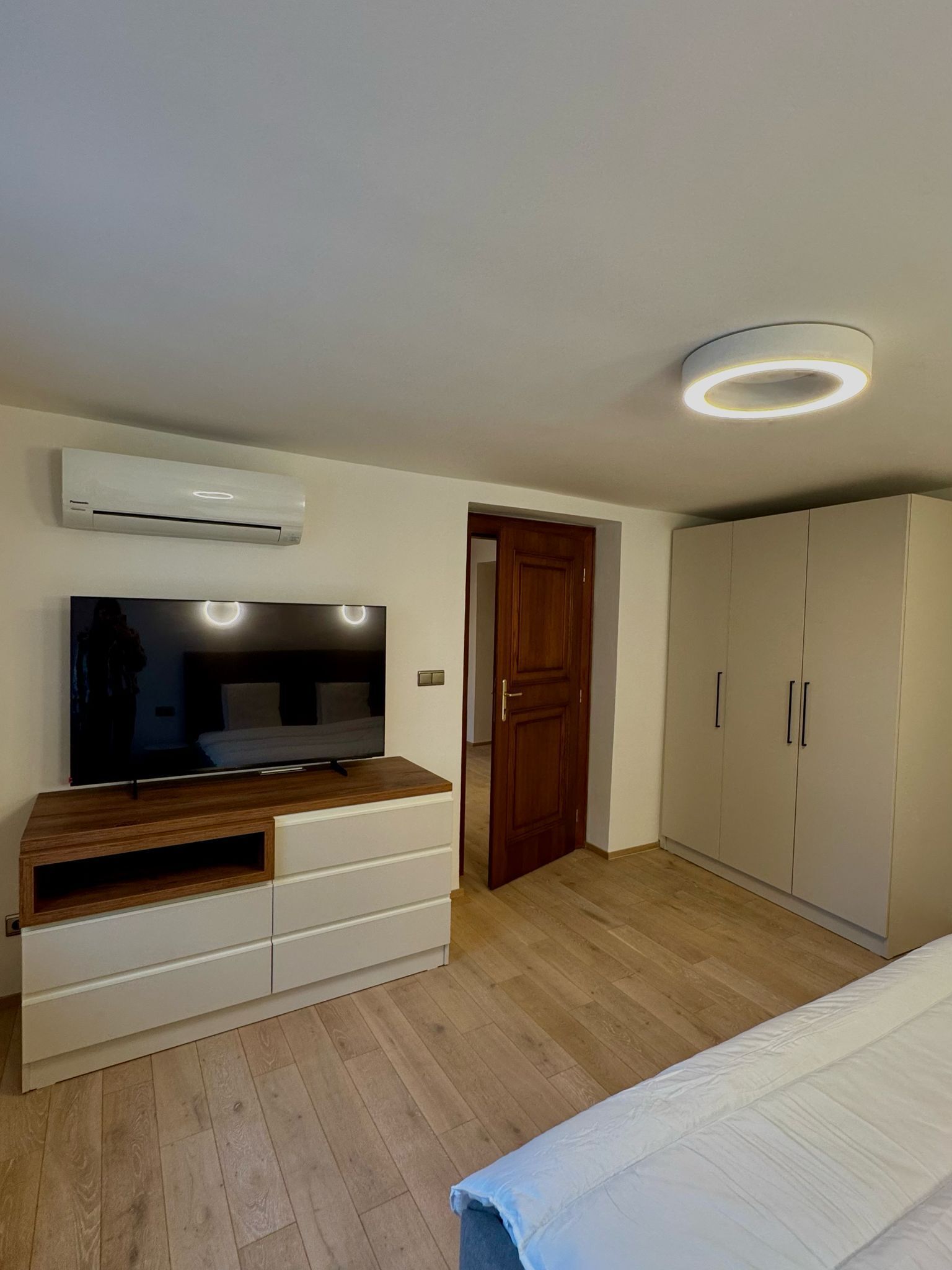 Un dormitorio con televisión sobre un mueble de madera, un armario y una lámpara en el techo.