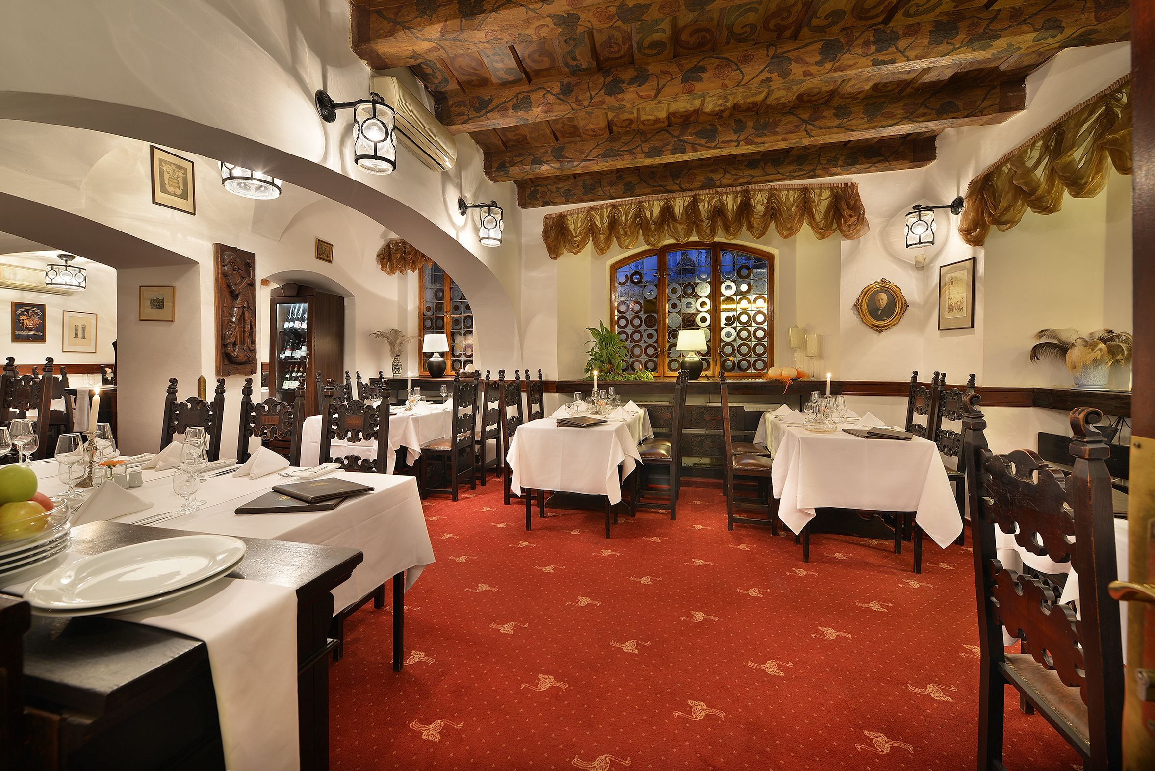 Un comedor con mesas dispuestas para el servicio, sillas de madera y un suelo cubierto de alfombra roja.