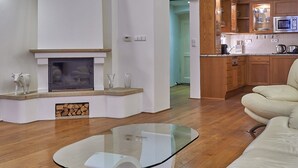 A modern living room with a glass coffee table, a fireplace, and a kitchen area with wooden cabinets and a microwave. - Hotel U Tri Pstrosu (Prague)