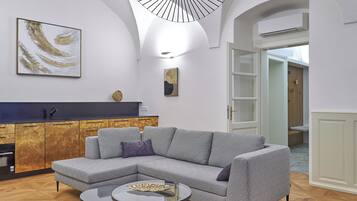 Una sala moderna con un sofá seccional, una mesa de centro de vidrio y una cocina con encimera oscura y armarios de madera.