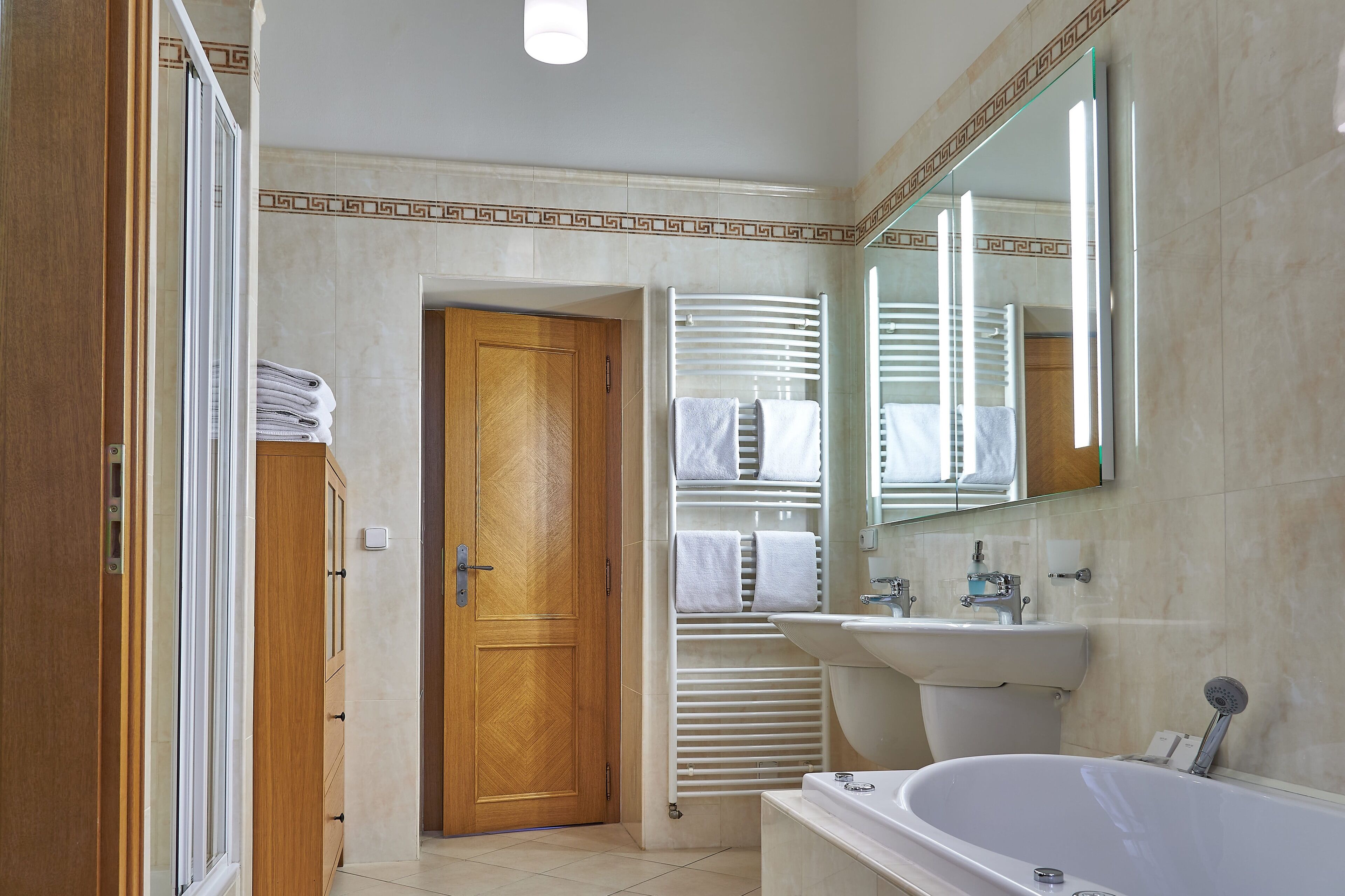 Une salle de bain moderne avec une porte en bois, un lavabo blanc, une baignoire et un porte-serviettes.