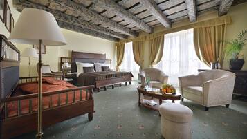 Quarto tradicional com cama de madeira, um espaço de estar com mesa de centro e uma janela grande com cortinas.