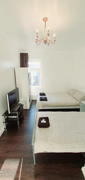 A hotel room with two beds, a TV, a desk, and a chandelier. - Regent Guest House Burnley (Burnley)