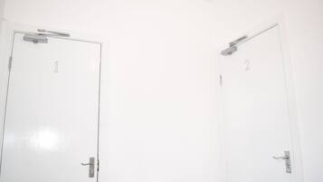 Dos puertas blancas con manijas numeradas, un radiador y una lámpara fijada a la pared.