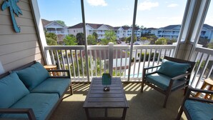 A balcony with a wooden table, two cushioned chairs, and a sofa.