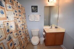 Ein Badezimmer mit einer Duschvorhang mit Seefahrt-Motiv, einer Toilette, einem Waschbecken mit Spiegel und einem Schrank.
