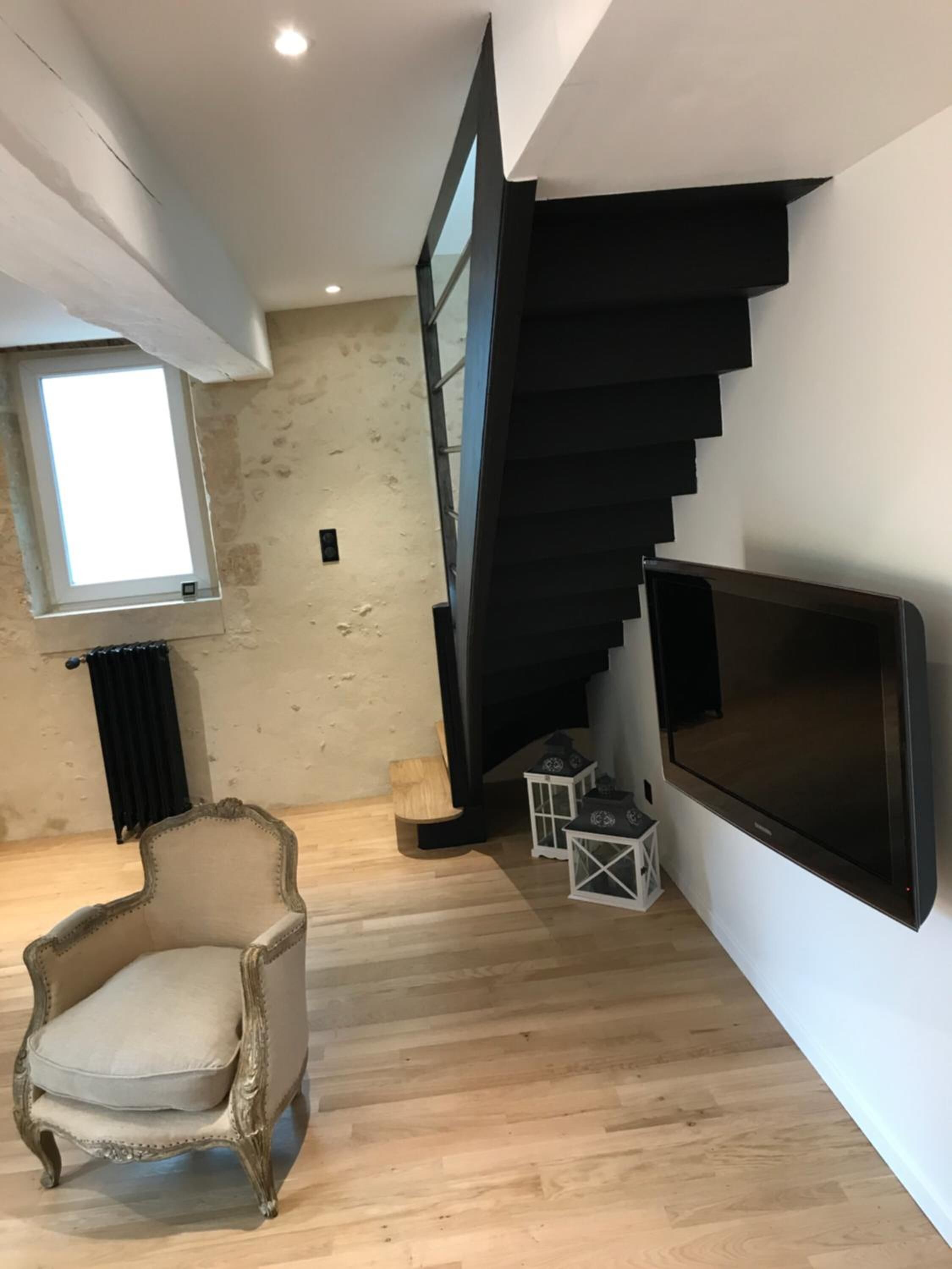 A modern interior with a wooden floor, a classic armchair, a large flat-screen TV, and a black spiral staircase.