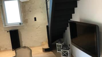 A modern interior with a wooden floor, a classic armchair, a large flat-screen TV, and a black spiral staircase.