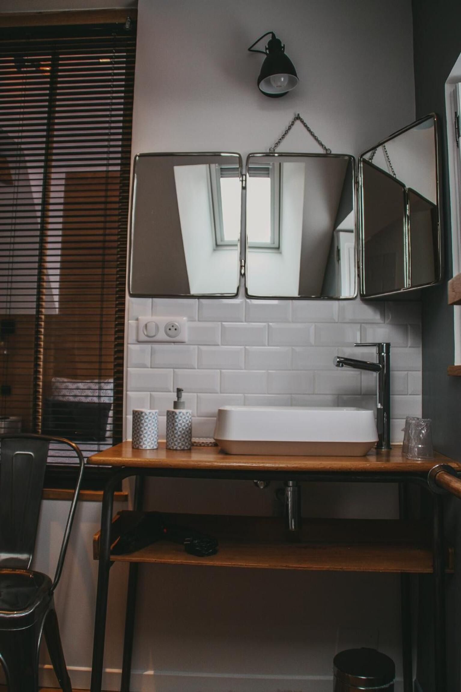 Een kleine badkamer met een witte betegelde spatwand, een houten wastafelmeubel, een enkele wastafel en een spiegel met een ketting.