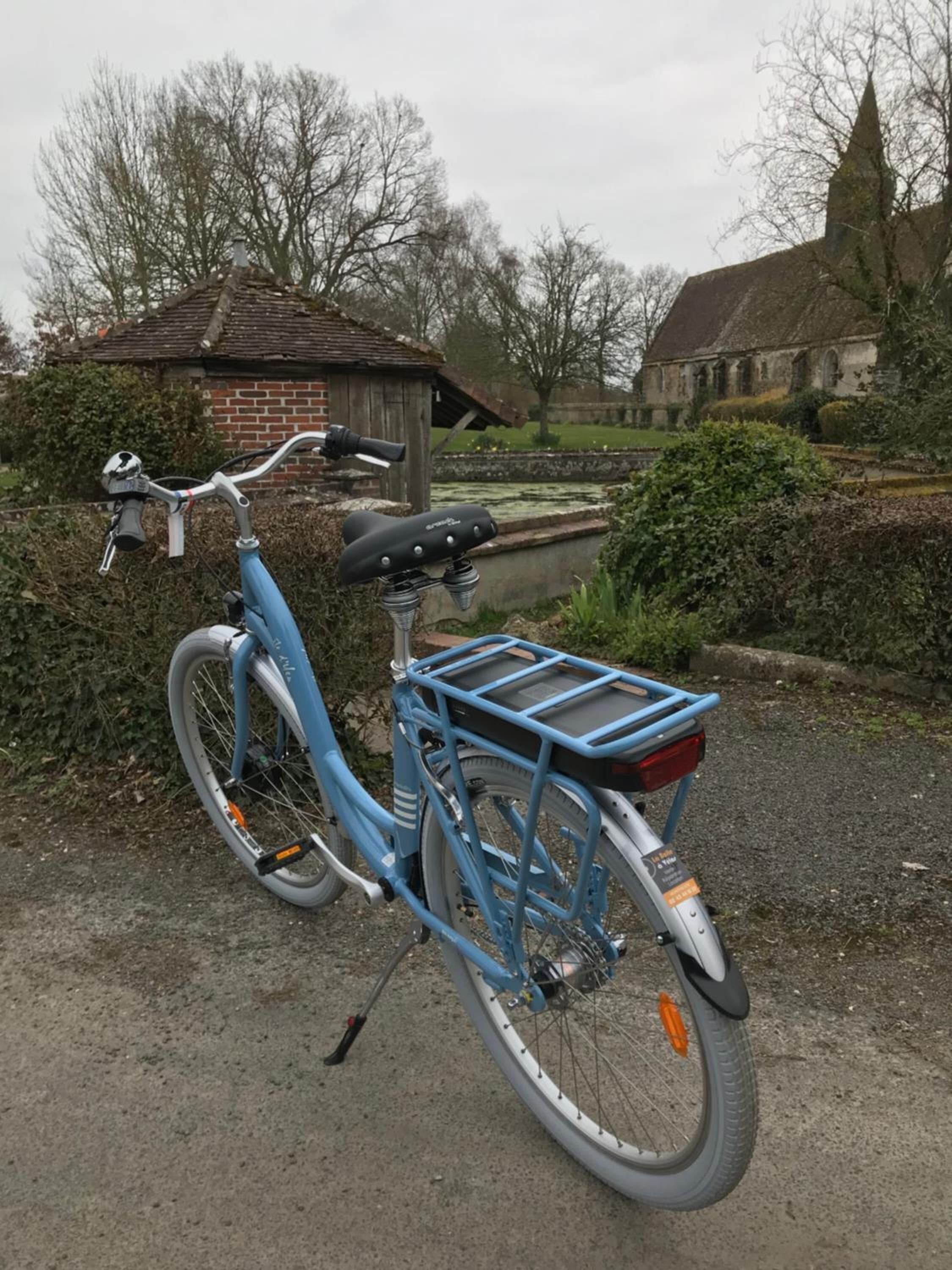 Ein blaues Fahrrad steht auf einem Schotterweg, mit Korb und Gepäckträger.