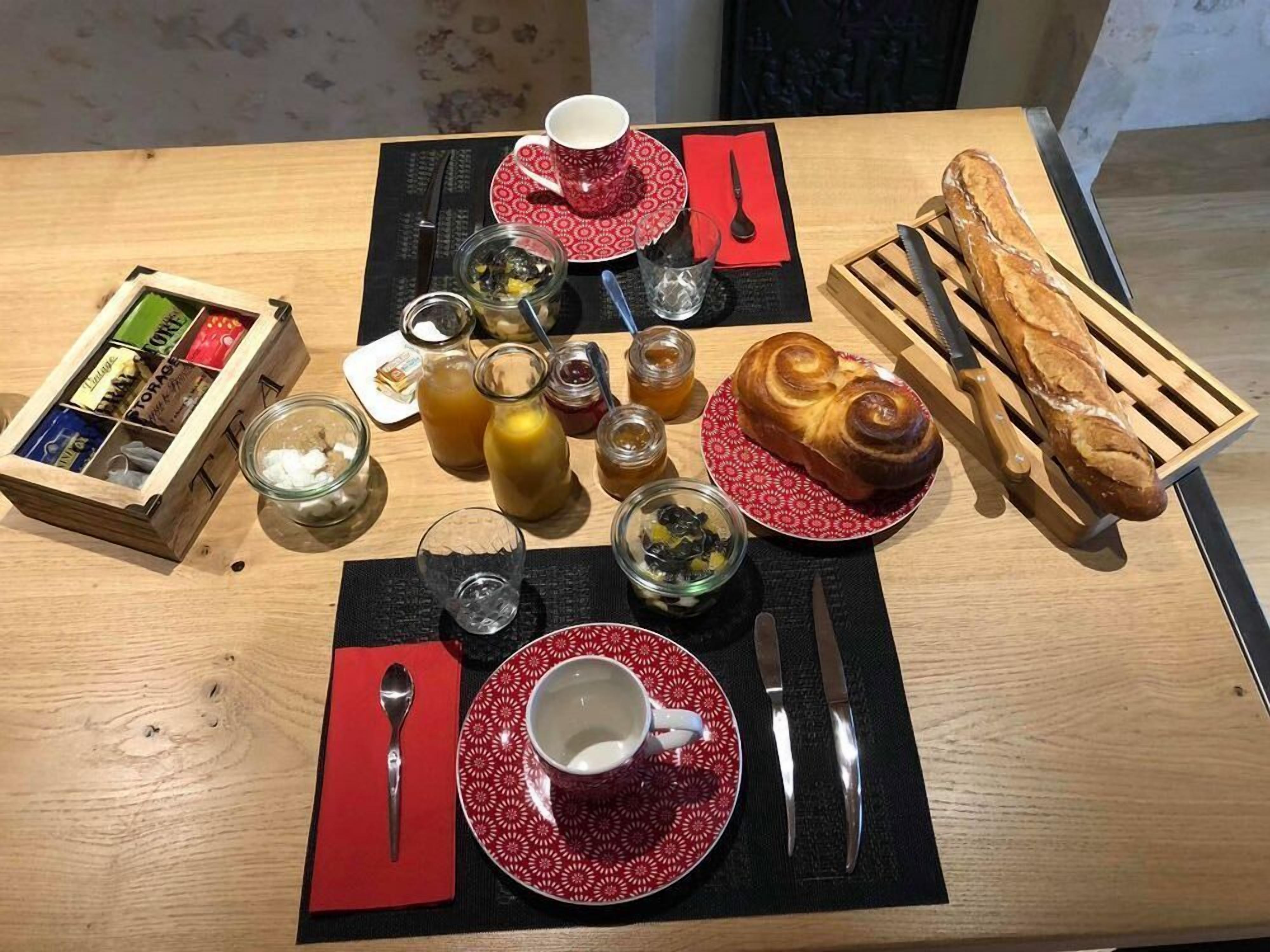 A breakfast setting with a croissant, bread, tea, and condiments on a wooden table.