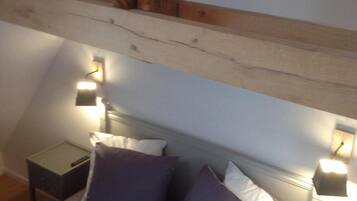 A bedroom with a bed, two nightstands, and a wooden ceiling beam.