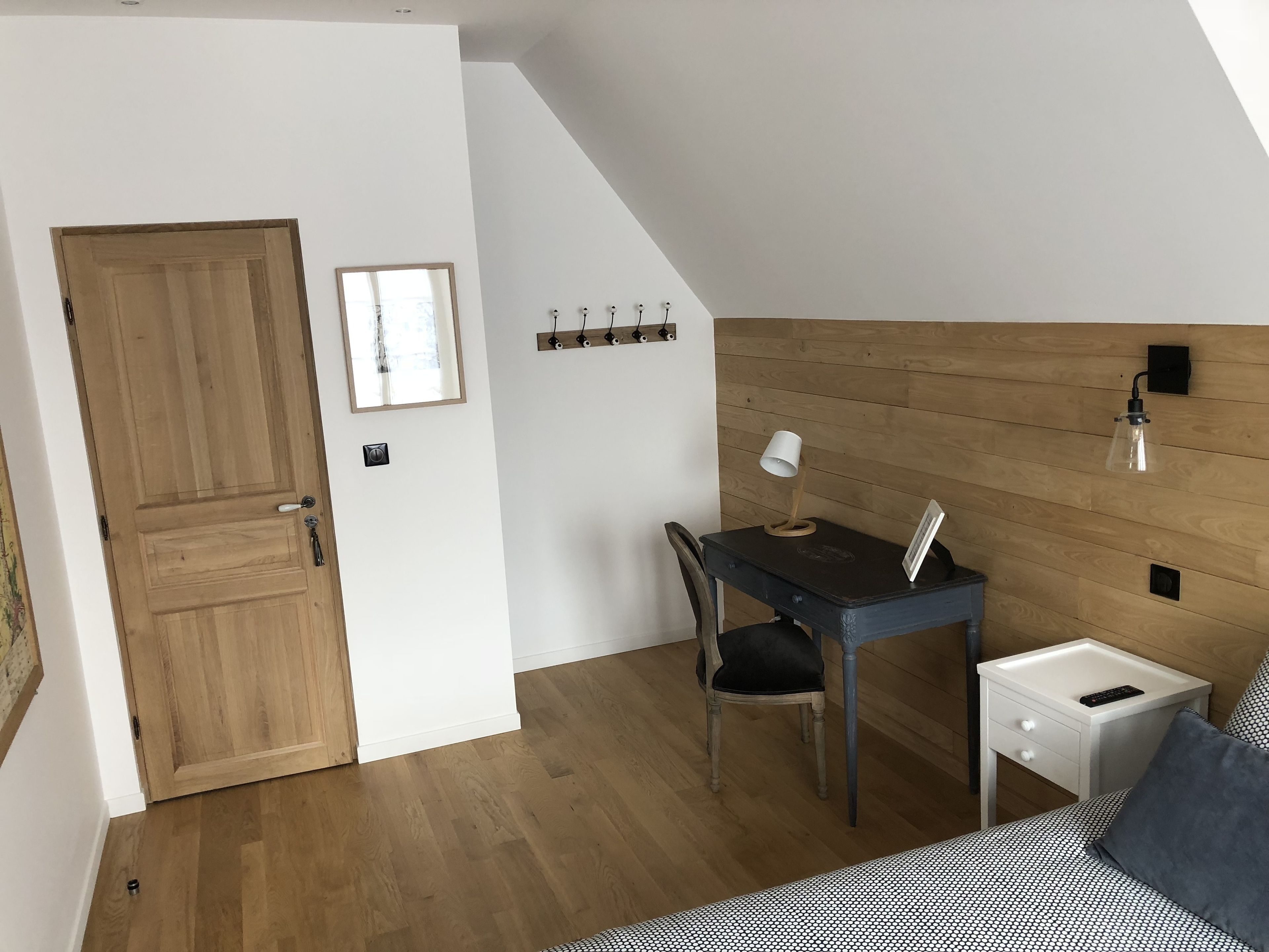 Una habitación pequeña y acogedora con una puerta de madera, un escritorio con una silla, una mesita de noche y una cama con una colcha estampada.