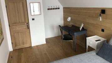 Una habitación pequeña y acogedora con una puerta de madera, un escritorio con una silla, una mesita de noche y una cama con una colcha estampada.
